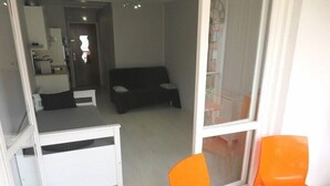 A room with a black sofa, a white desk, and two orange chairs. - BEAU STUDIO RENOVE ENTRE PLAGE ET CENTRE PORT AVEC PARKING (LE CAP D AGDE)