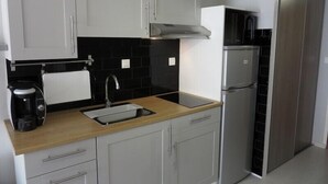 A modern kitchen with white cabinets, a black backsplash, a stainless steel refrigerator, and a coffee maker. - BEAU STUDIO RENOVE ENTRE PLAGE ET CENTRE PORT AVEC PARKING (LE CAP D AGDE)