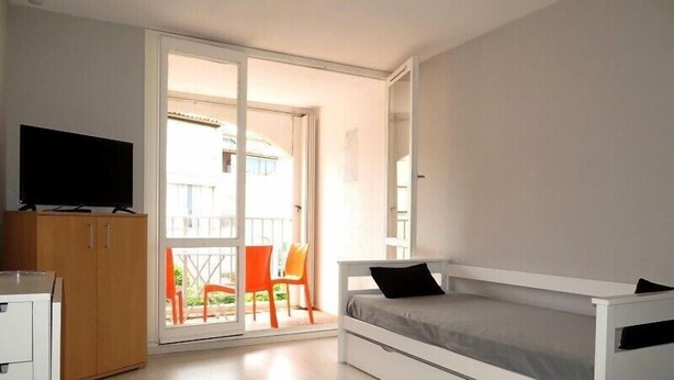 A bedroom with a bed, a TV, a wardrobe, and a balcony with chairs. - BEAU STUDIO RENOVE ENTRE PLAGE ET CENTRE PORT AVEC PARKING (LE CAP D AGDE)