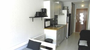 A compact living space with a kitchenette, a bed with pillows, and a door with a unique design. - BEAU STUDIO RENOVE ENTRE PLAGE ET CENTRE PORT AVEC PARKING (LE CAP D AGDE)