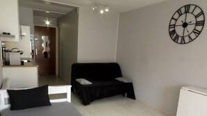 A modern bedroom with a bed, a black sofa, a large wall clock, and a white radiator. - BEAU STUDIO RENOVE ENTRE PLAGE ET CENTRE PORT AVEC PARKING (LE CAP D AGDE)