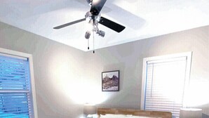 A bedroom with a bed, a ceiling fan, a nightstand, a lamp, and a patterned rug. - Skots Villa Bottom East. Centrally located near Sanford Medical Center & Midco. (Sioux Falls)