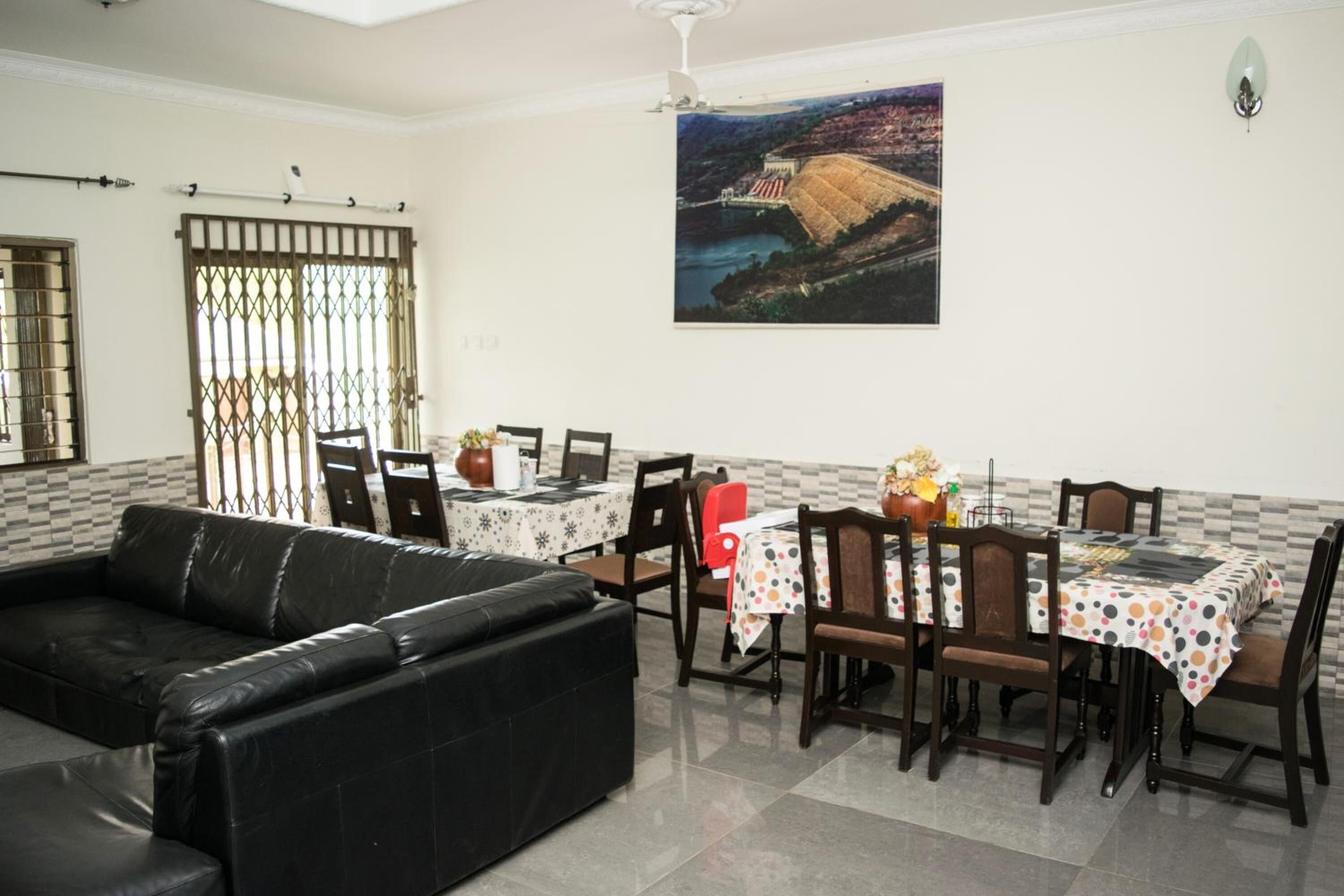 A dining area with a table set for four, a black leather sofa, and a large painting on the wall.