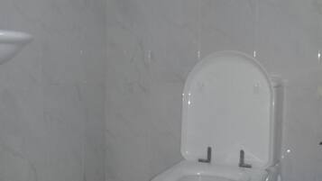 Een badkamer met een toilet, een blauwe prullenbak en een witte vloer.