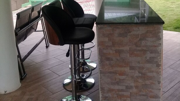 A covered outdoor area with a bar counter, two bar stools, and a seating area with chairs. - 3A's Guest House (Akosombo)