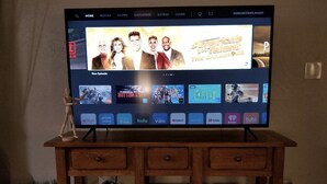 Una TV a schermo piatto su un supporto in legno con interfaccia Netflix che mostra diverse serie TV e film.