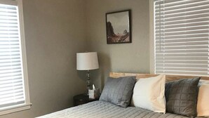 Un letto rifatto con copriletto trapuntato, una lampada da comodino e un quadro appeso al muro.