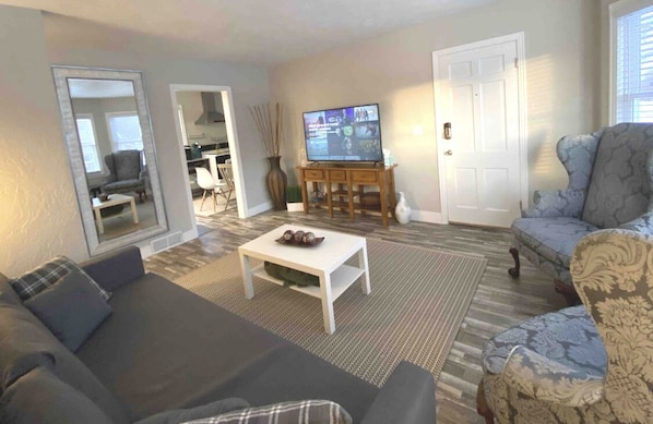 Un salon comprenant un canapé, un fauteuil, une table basse, un téléviseur et une porte.