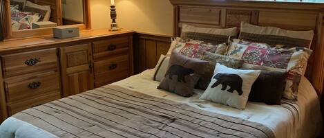 A bedroom with a large bed, a dresser, a mirror, and a window with curtains.