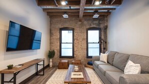 A modern living room with a large flat-screen TV, a wooden coffee table, a grey sofa, and a rustic brick wall. - Downtown Spokane Urban Retreat with King Bed! (Spokane)