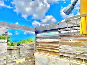 A wooden structure with a metal railing, a clear blue sky, and greenery in the background.