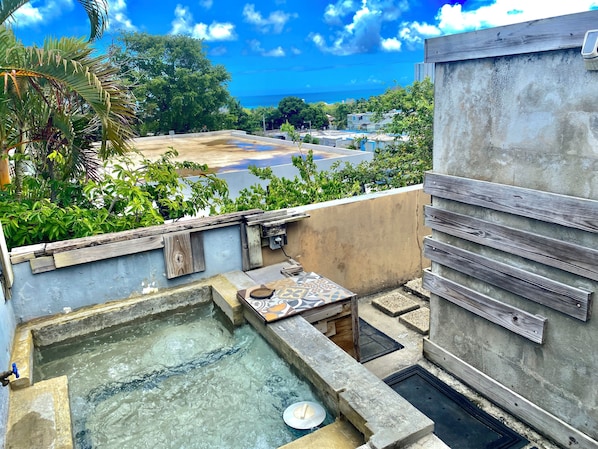 A rooftop with a small pool, a wooden bench, and a view of the ocean and buildings.