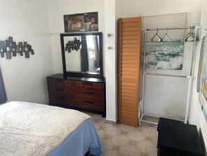 A bedroom with a bed, dresser, mirror, wooden panel, and a wall with a painting.