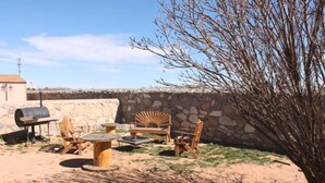 Un área de patio al aire libre con un muro de piedra, una parrilla de barbacoa y mobiliario de madera.