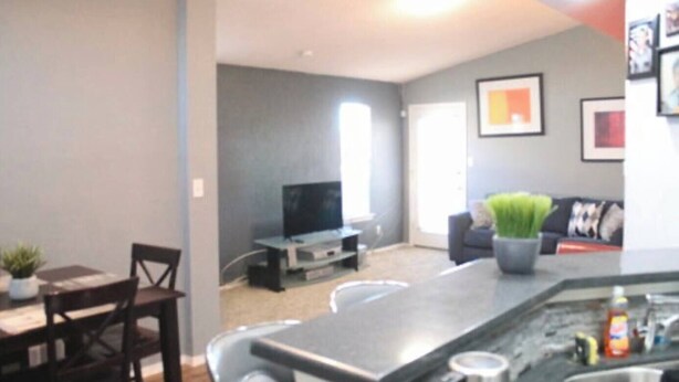 Una sala de estar moderna con televisor de pantalla plana, un comedor con mesa y sillas, y una cocina con barra.