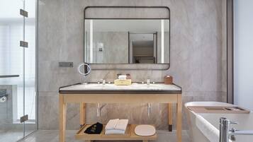 A modern bathroom with a large mirror, a double sink, a bathtub, and a wooden vanity.