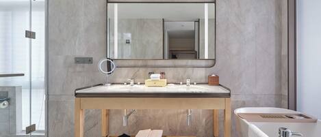 A modern bathroom with a large mirror, a double sink, a bathtub, and a wooden vanity.