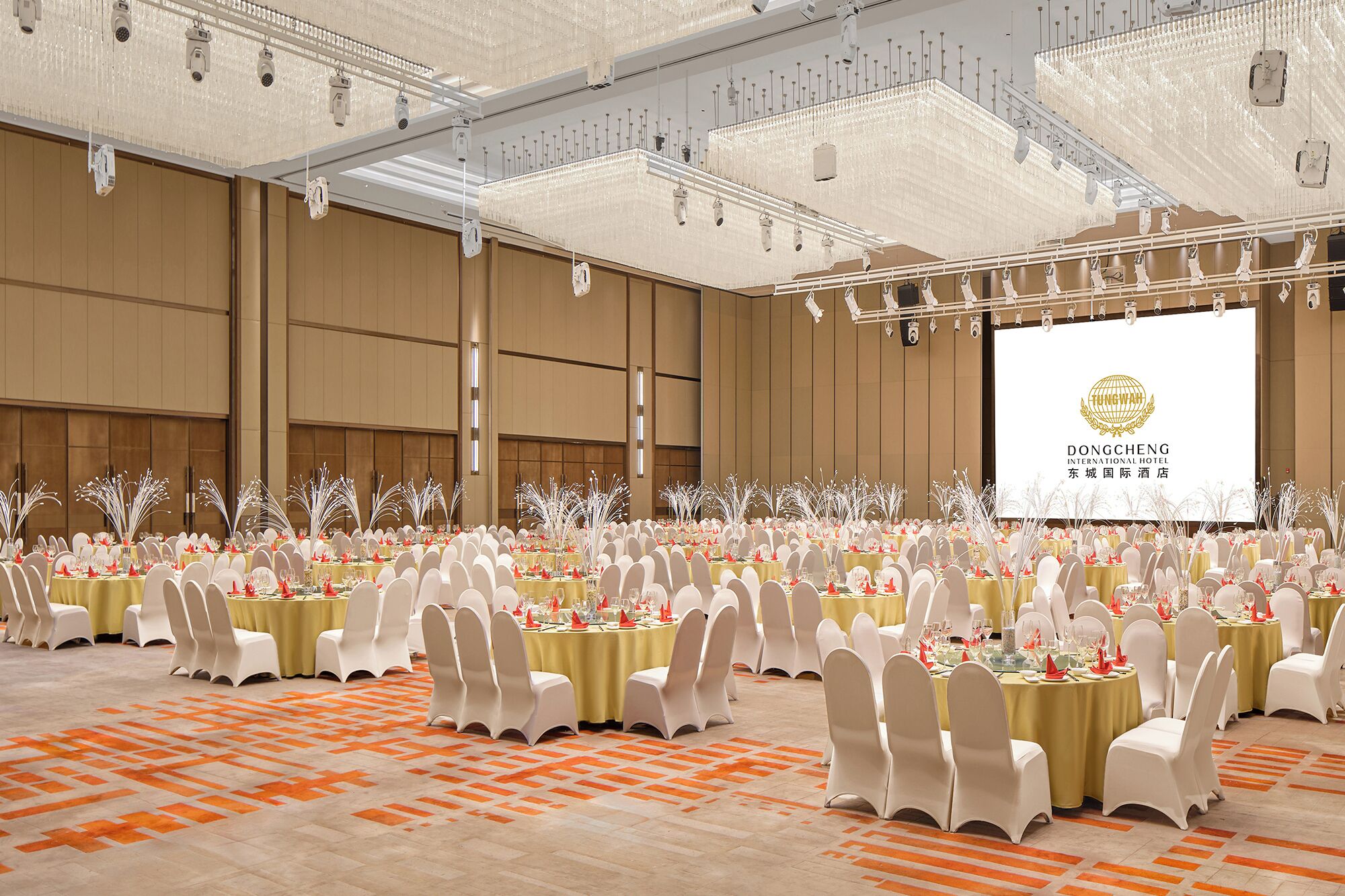 A large banquet hall with rows of round tables, white chairs, and a projection screen displaying the Dongcheng International Hotel logo.