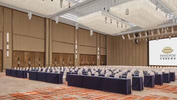A large conference room with rows of tables and chairs, a large screen, and a chandelier.