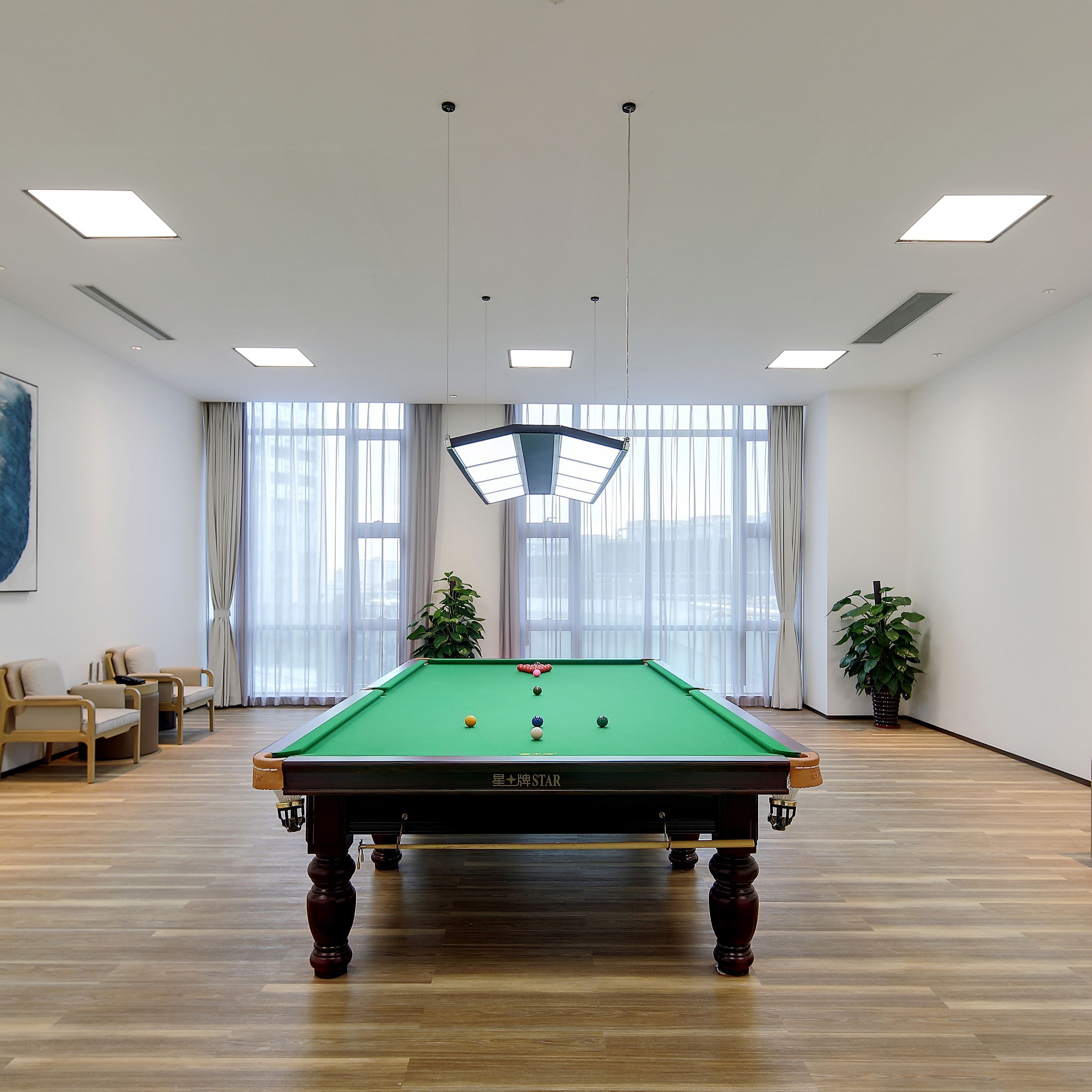 A pool table in a room with large windows, a sofa, and a potted plant.