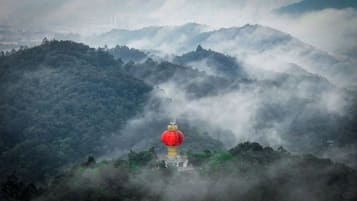 A mountainous landscape with a red lantern on a yellow pillar, surrounded by dense forest and mist.
