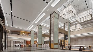 A spacious lobby with a high ceiling, modern lighting fixtures, and a central staircase.