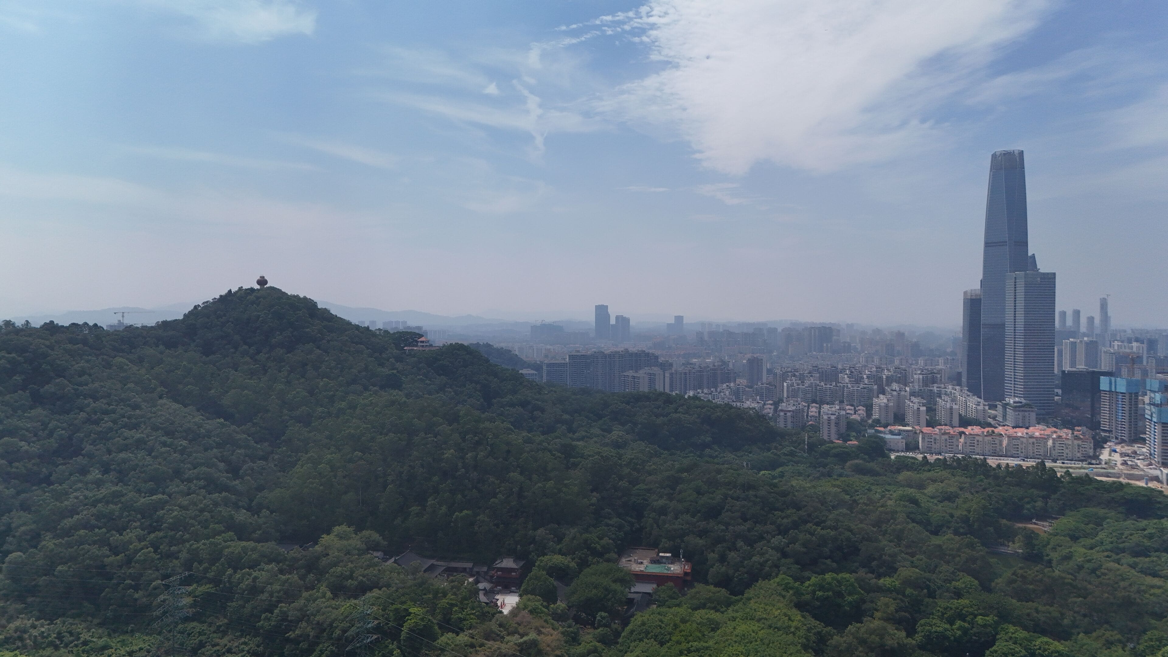 Un paysage urbain caractérisé par un gratte-ciel imposant, des collines verdoyantes et un mélange de bâtiments résidentiels et commerciaux.