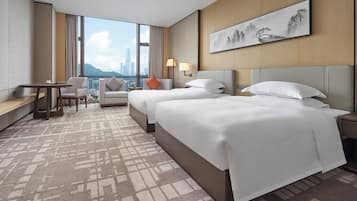 A hotel room with two beds, a desk, and a view of a cityscape.