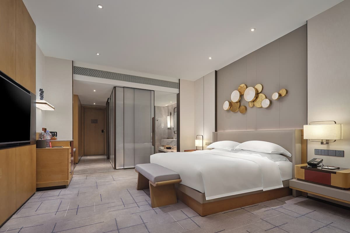 A modern hotel room with a large bed, a TV, a desk, and a bathroom.