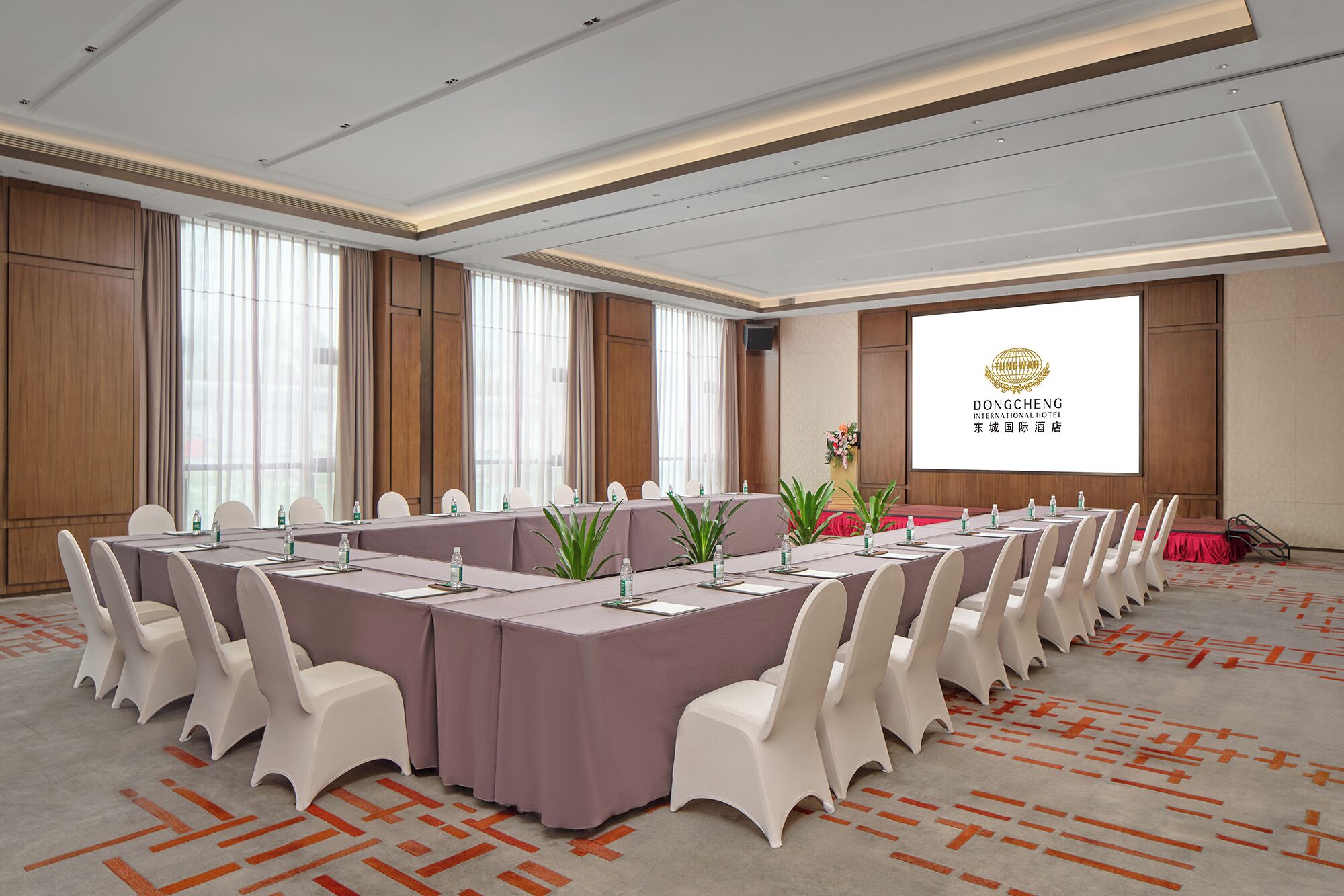 A conference room with long tables, white chairs, and a projector screen displaying the Dongcheng International Hotel logo.