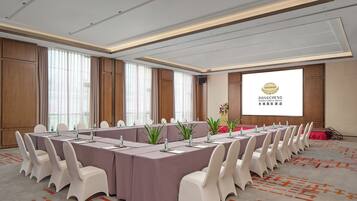 A conference room with long tables, white chairs, and a projector screen displaying the Dongcheng International Hotel logo.
