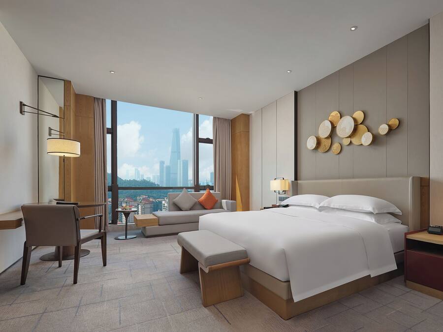 A modern hotel room with a large bed, a desk, a chair, and a TV.