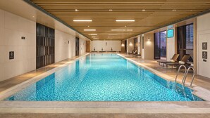 A long indoor swimming pool with tiled walls and ceiling, equipped with lounge chairs and a ladder. - Dongguan Dongcheng International Hotel (Dongguan)
