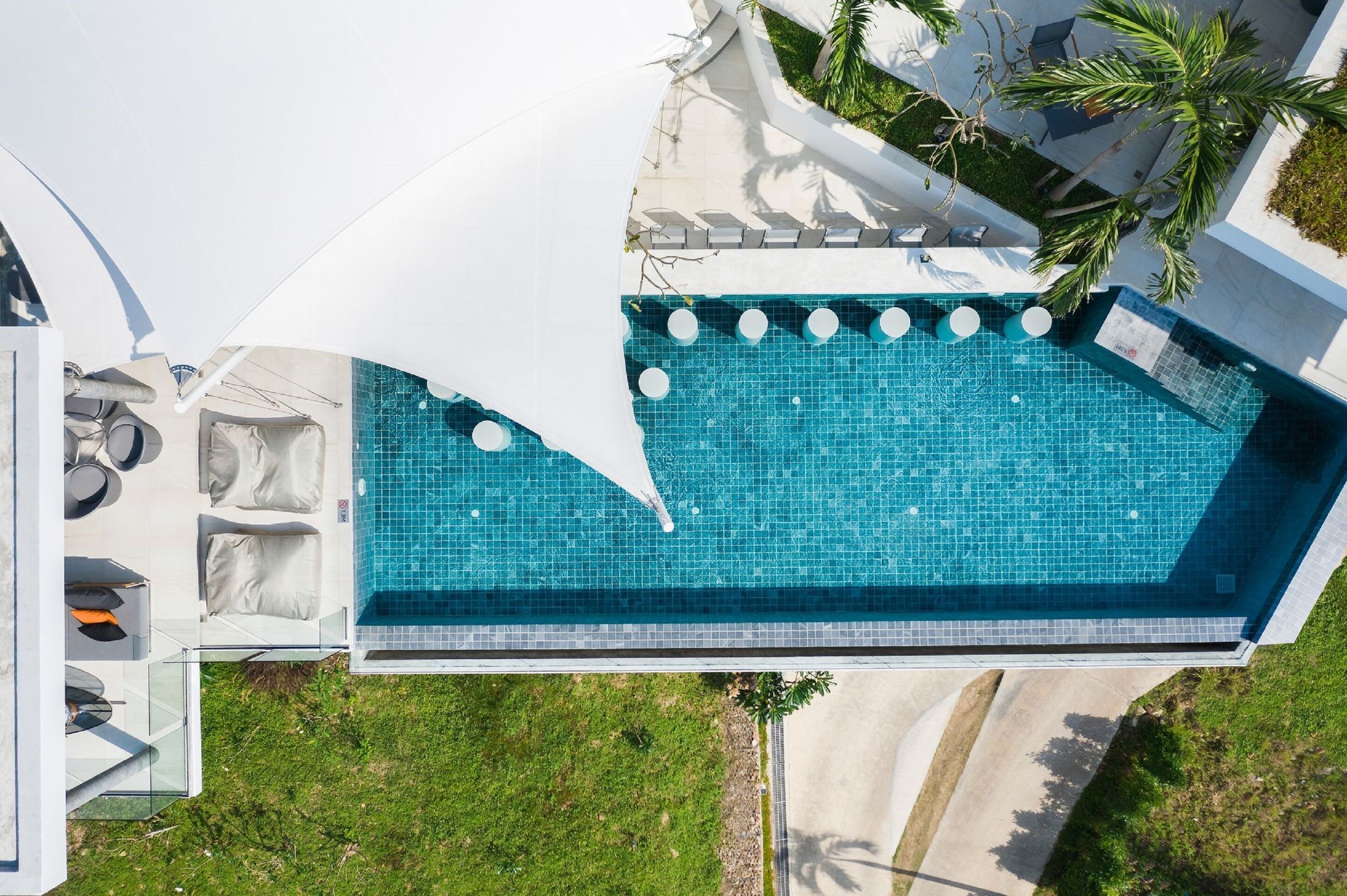 A rooftop swimming pool with a clear blue tile design, surrounded by outdoor seating and a white canopy.