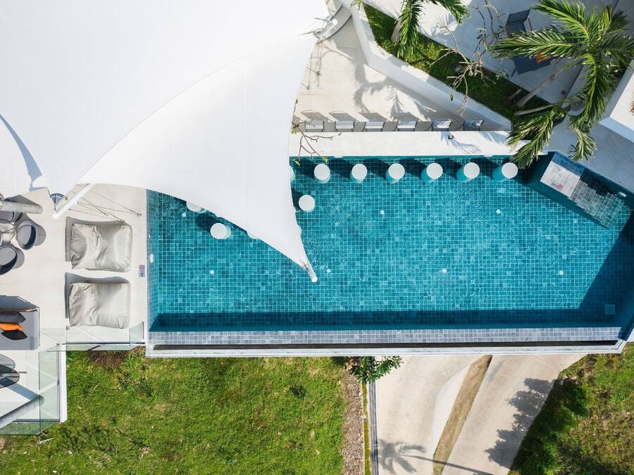 A rooftop swimming pool with a clear blue tile design, surrounded by outdoor seating and a white canopy.