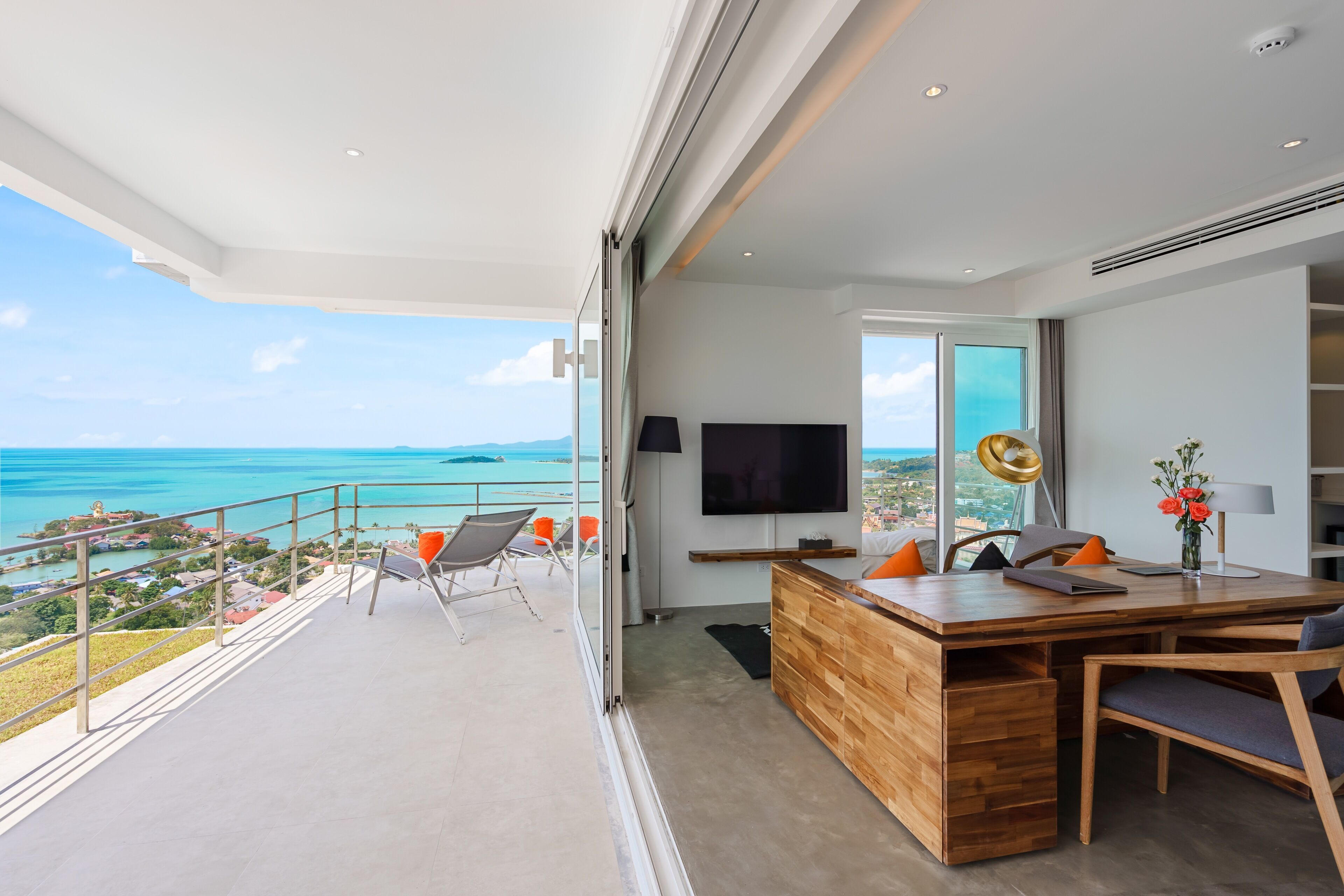 A modern living room with a wooden desk, a flat-screen TV, and a view of the ocean.