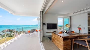 A modern living room with a wooden desk, a flat-screen TV, and a view of the ocean.