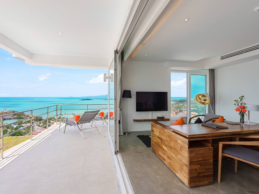 A modern living room with a wooden desk, a flat-screen TV, and a view of the ocean.