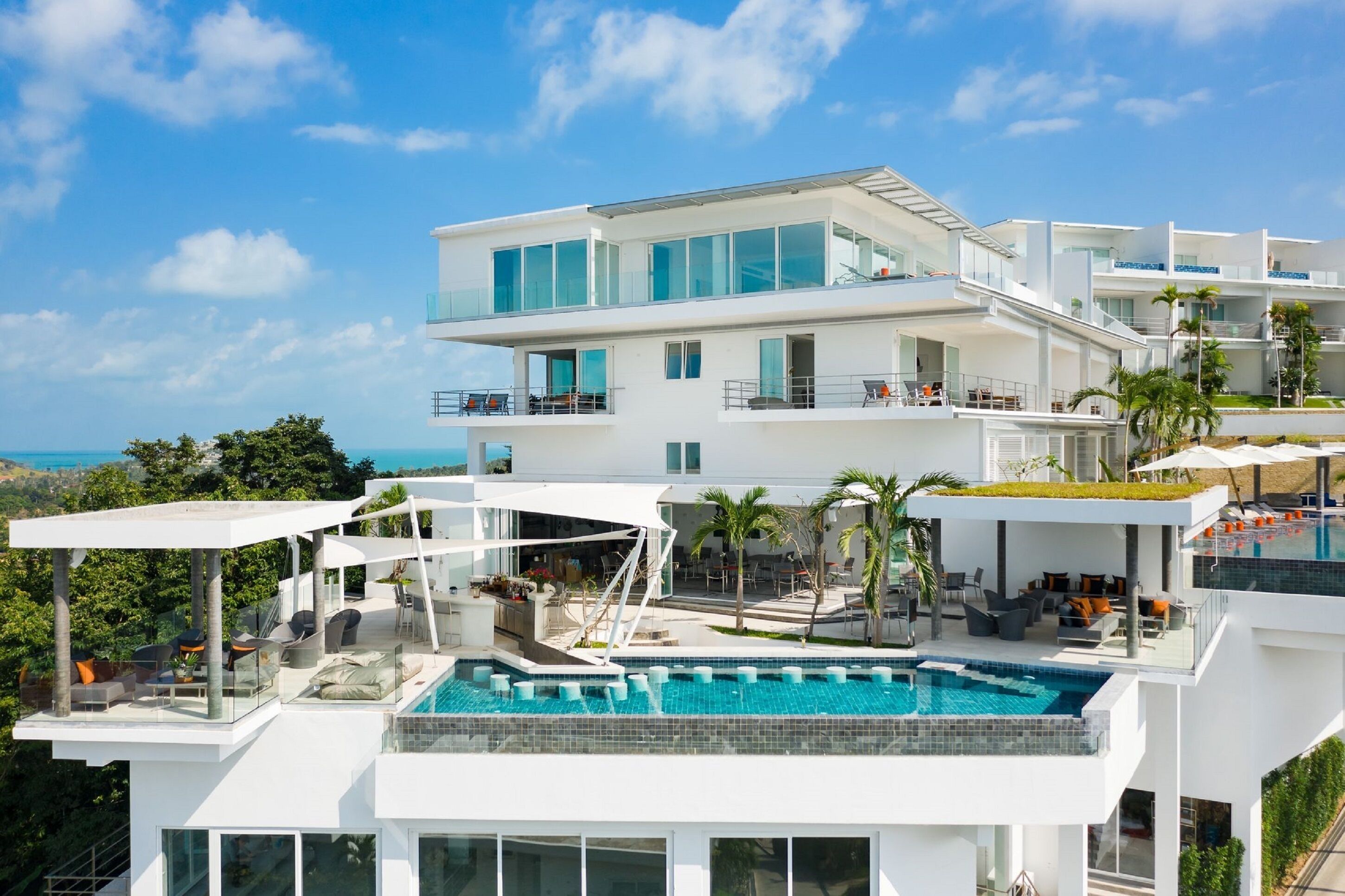 Un hotel moderno de varios pisos con piscina infinita en la azotea, zonas de estar al aire libre y vistas al océano.