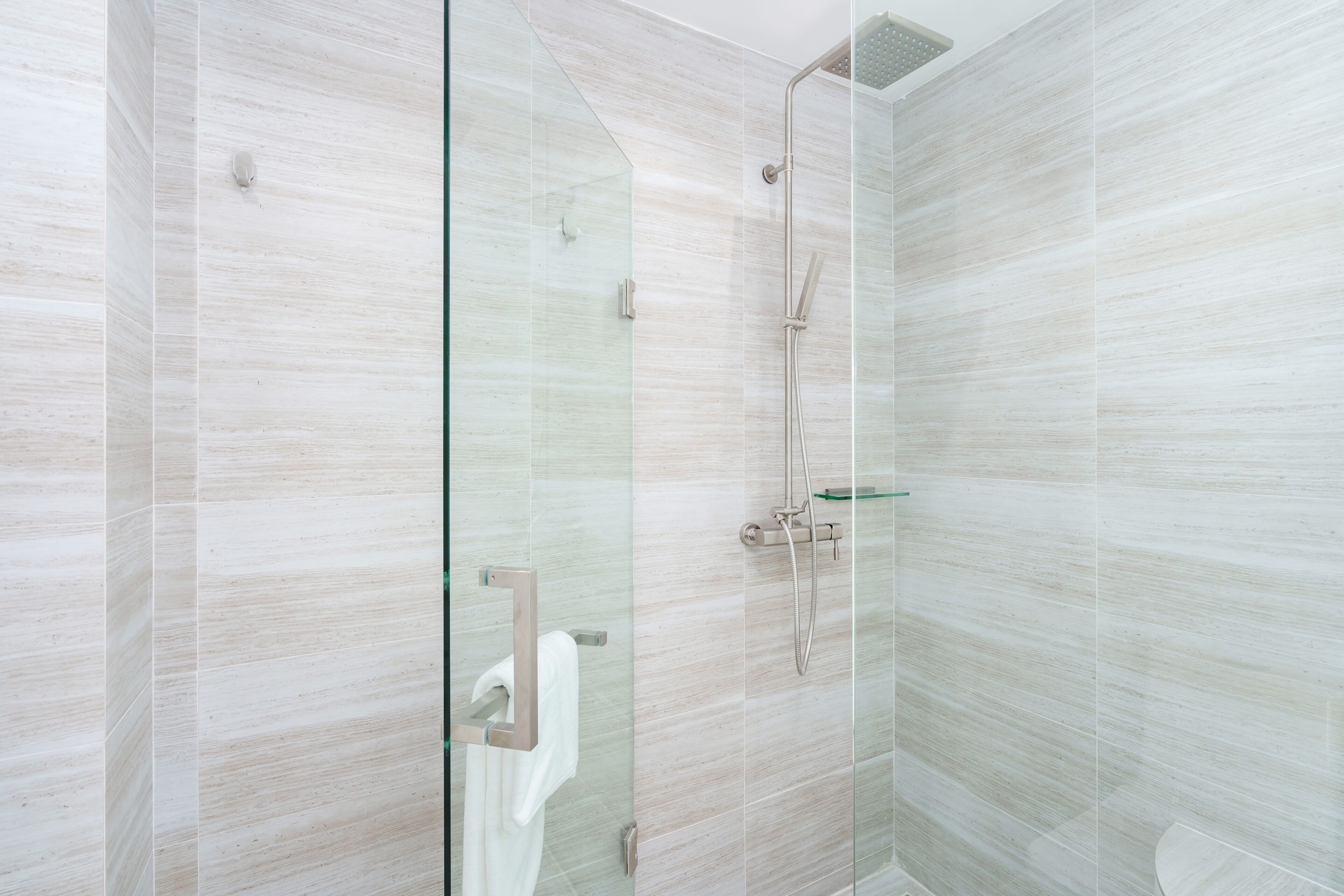 Una ducha moderna con puerta de vidrio, cabezal de ducha manual y grifo de mano.
