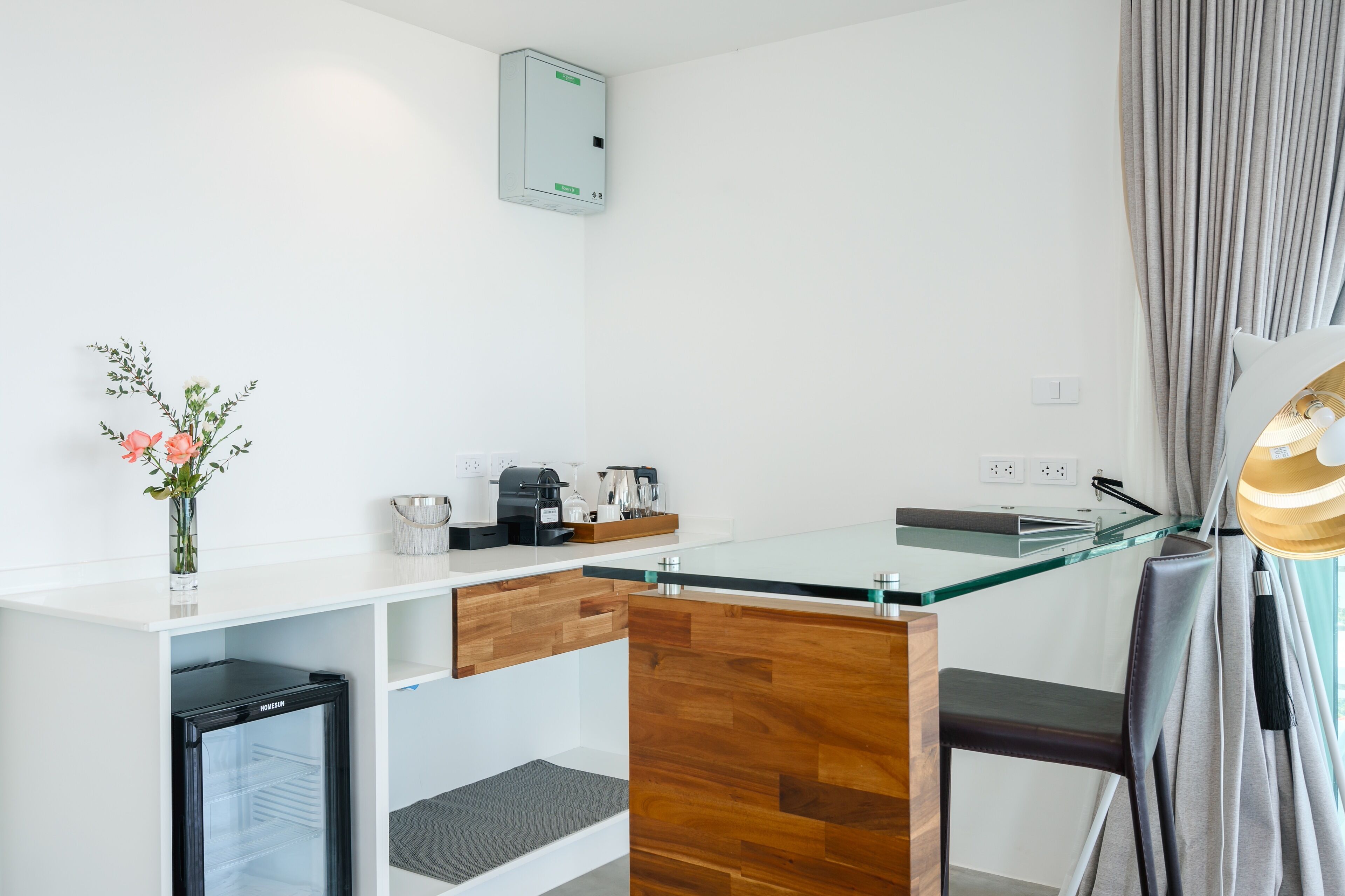 A modern kitchen with a glass countertop, wooden cabinets, a built-in mini-fridge, and a coffee station.
