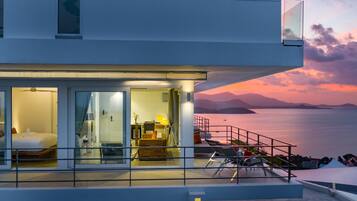 Een modern hotel met een balkon met uitzicht op een schilderachtig zee- en berglandschap bij zonsondergang.