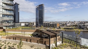Eine moderne Stadtlandschaft mit Hochhäusern, einem Uferweg und einer Holzterrasse mit Sitzgelegenheiten.