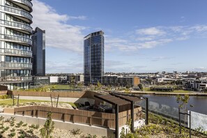 Un paysage urbain moderne avec de hauts immeubles, une promenade au bord de la rivière et une terrasse en bois dotée de sièges.