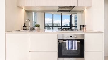 A modern kitchen with a built-in oven, stainless steel appliances, and a window overlooking a cityscape.