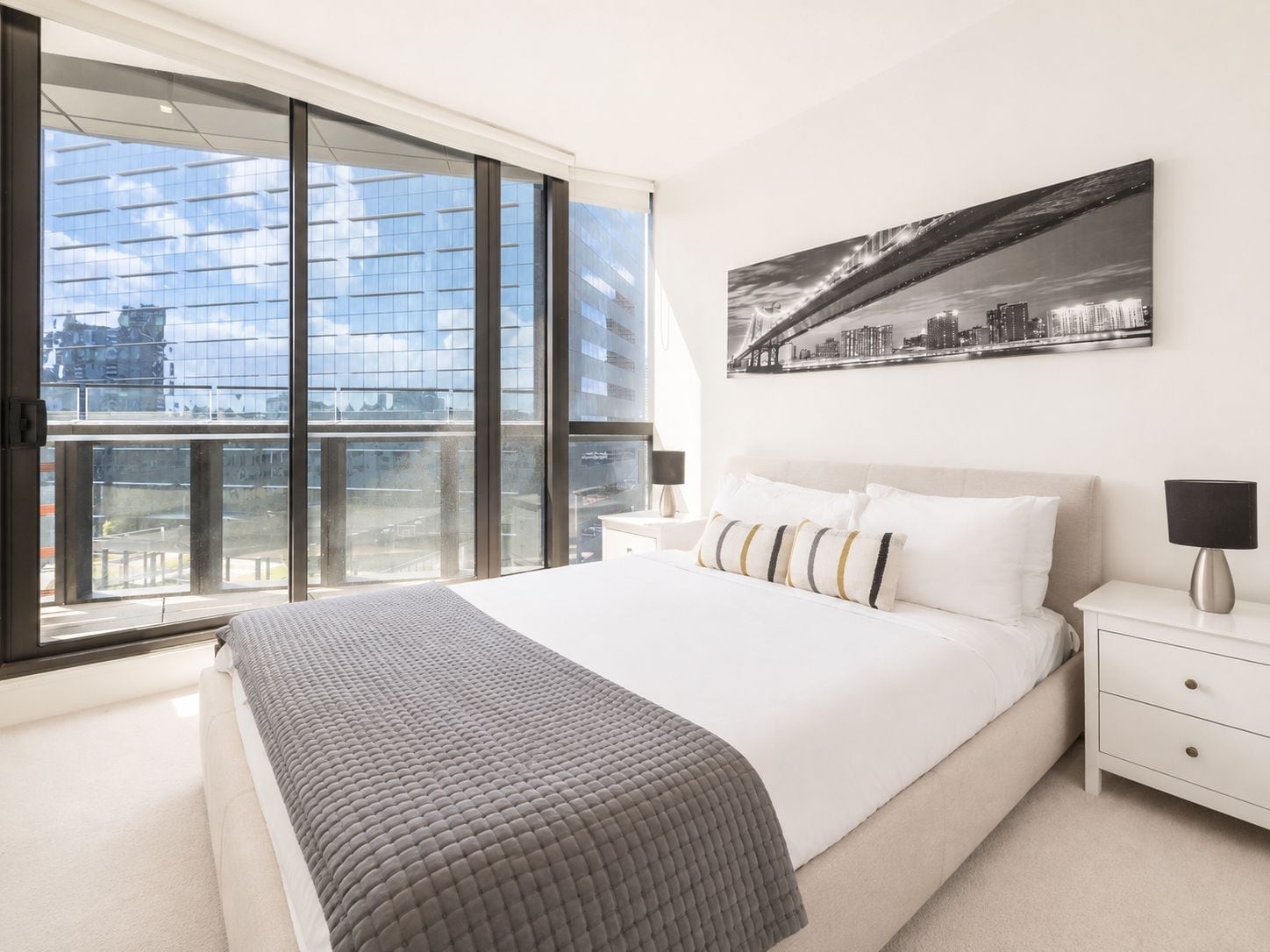 A modern bedroom with a large bed, a cityscape view, and a city skyline painting.