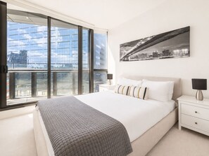Une chambre moderne avec un grand lit, une vue sur la ville et un tableau représentant le panorama urbain.