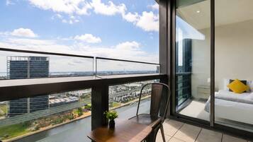 A balcony with a view of a river and cityscape, a dining area with a table and chairs, and a bedroom with a bed and a window.