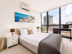 Ein modernes Hotelzimmer mit einem großen Bett, einem Schreibtisch und Blick auf die Stadt durch große Fenster.