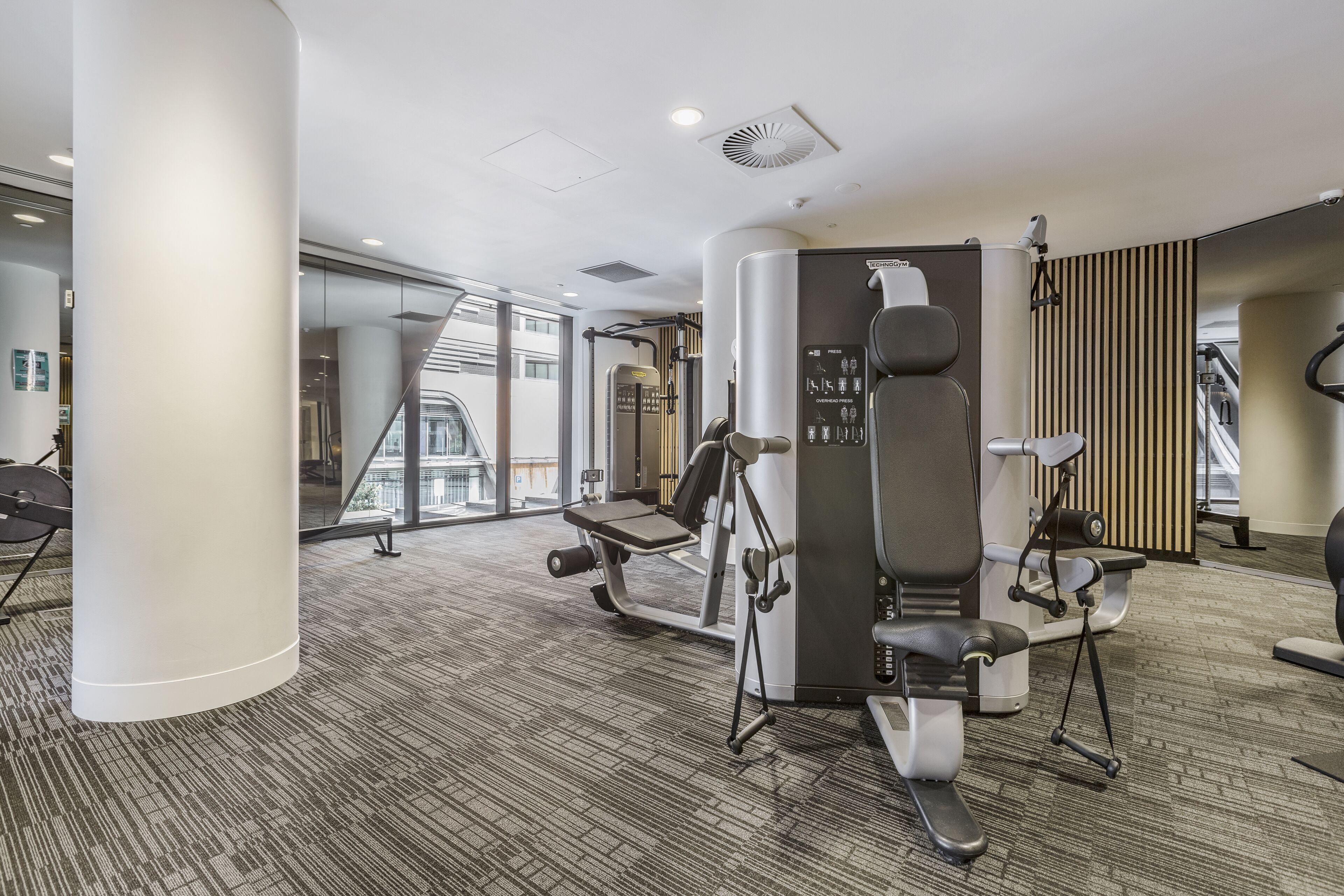 Een moderne sportschool met diverse trainingsapparaten, grote ramen en een vloerbedekking.